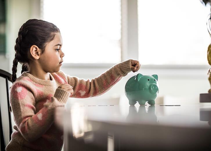 Girl (7 yrs) putting money in piggybank